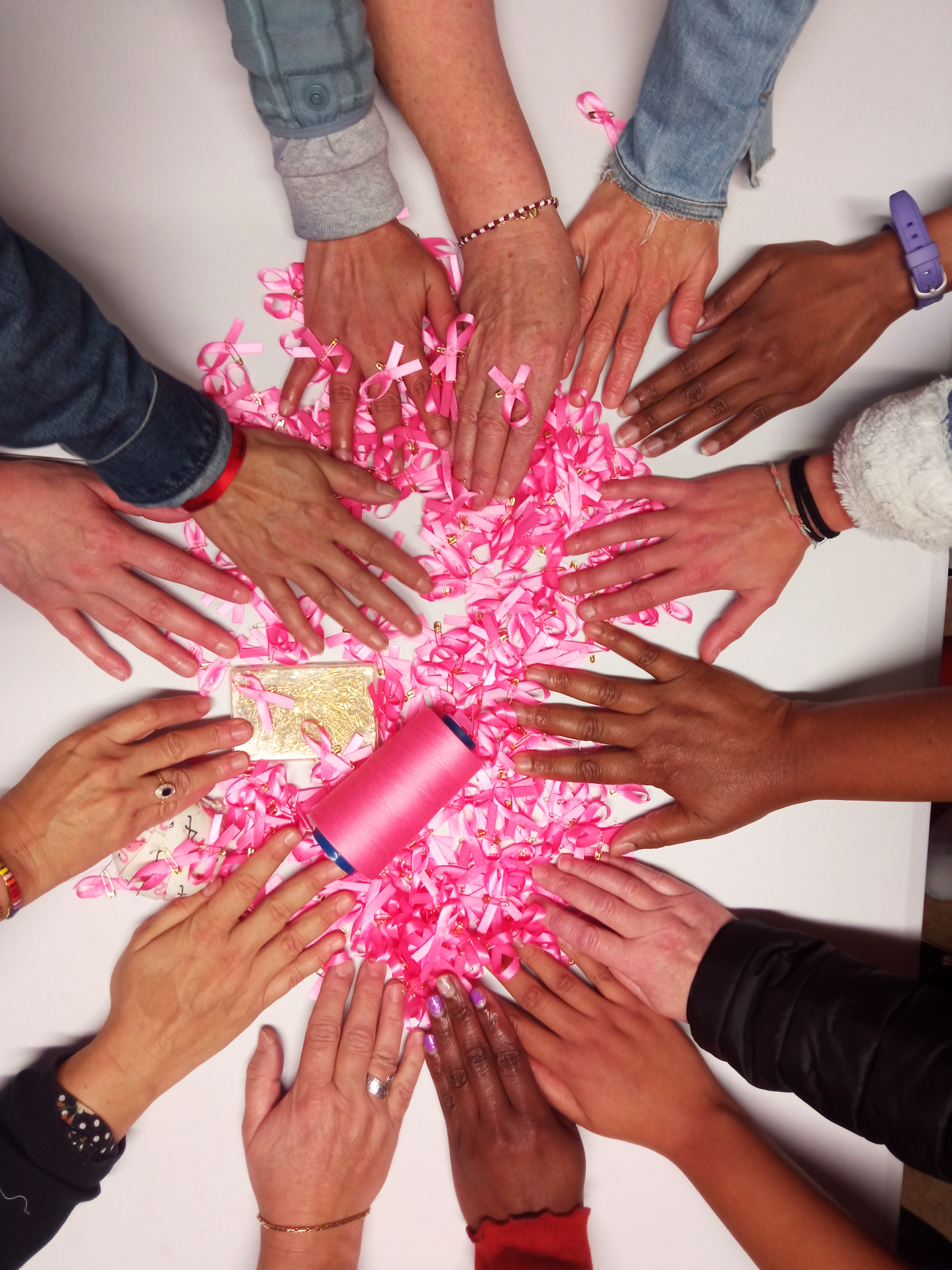 Photo prise au dessus d'une table, plusieurs mains se rejoignent au dessus de plusieurs rubans roses
