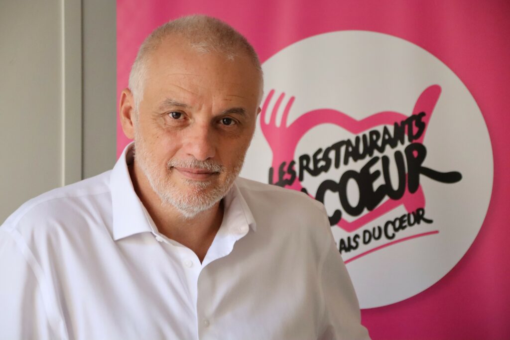 Portrait de Patrice Douret, président des Restaurant du coeur, devant le logo de l'association